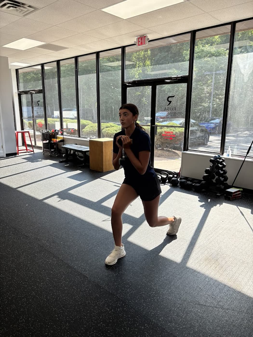 Patient performing a lunge in the clinic gym beside large windows