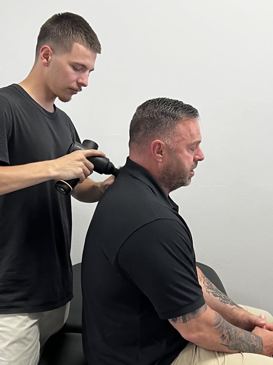 Therapist using a percussion massage device on a patient's shoulder