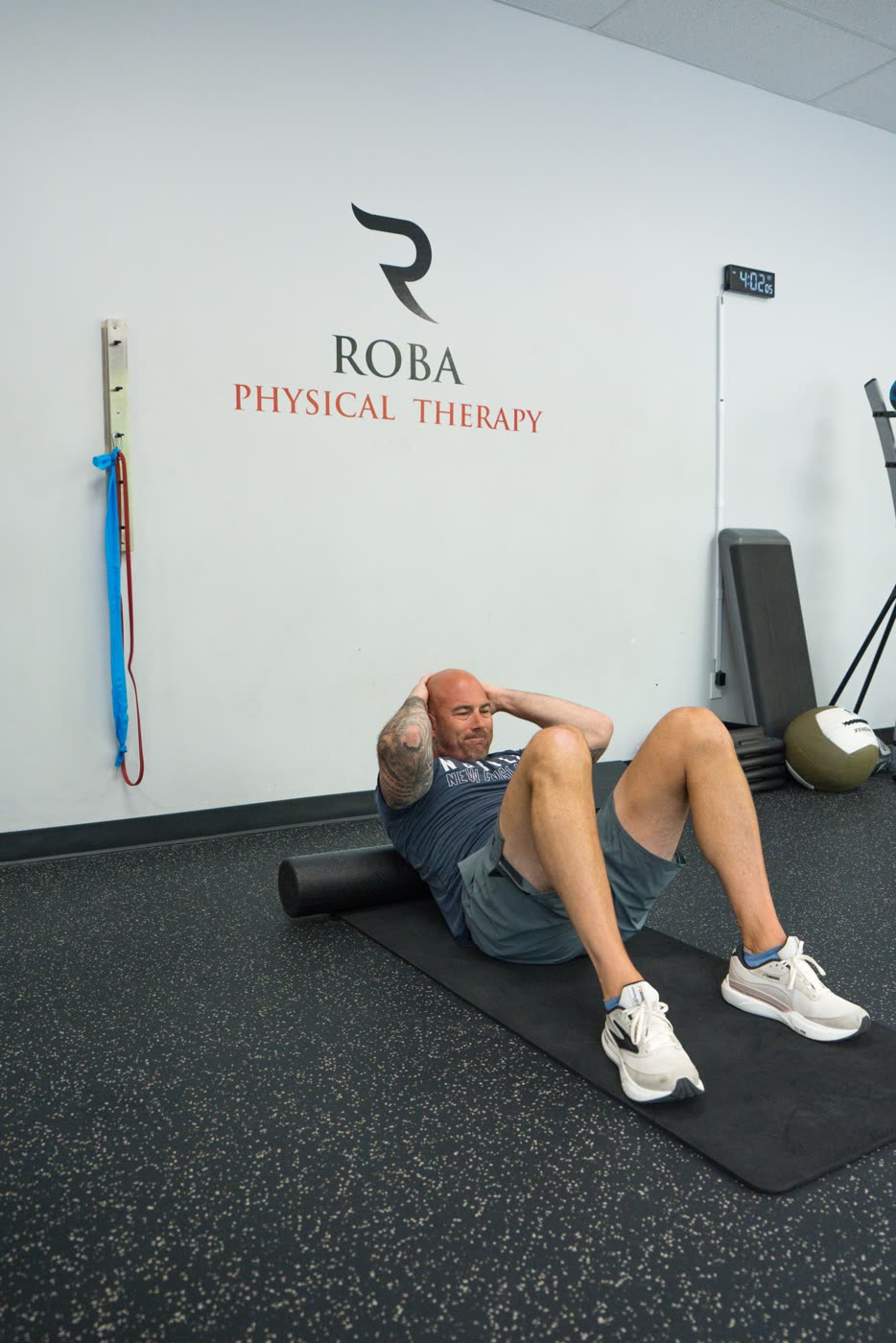 Patient doing a core exercise on a mat beneath the Roba Physical Therapy logo inside the clinic